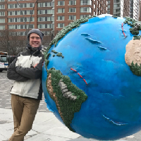 photograph of a smiling man leanig against a world sculpture